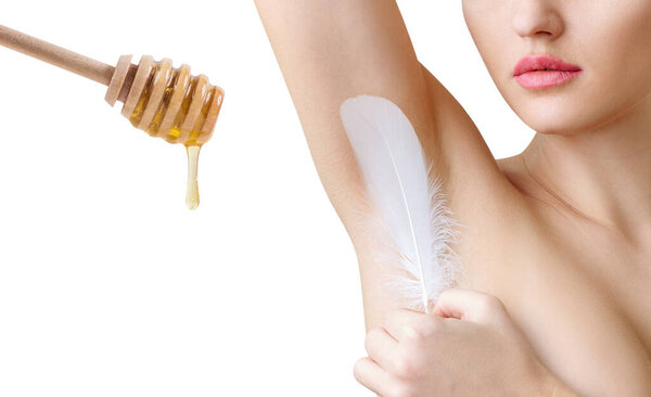 Woman holds feather near clean armpit and honey spoon.