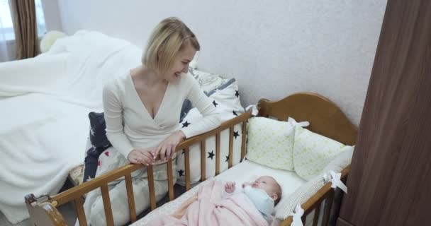 Junge Mutter sitzt in der Nähe der Krippe und blickt auf ihr Neugeborenes. — Stockvideo