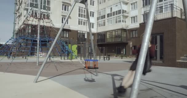 Mujer joven sonriente balanceándose en el columpio en el patio de recreo de la ciudad . — Vídeo de stock