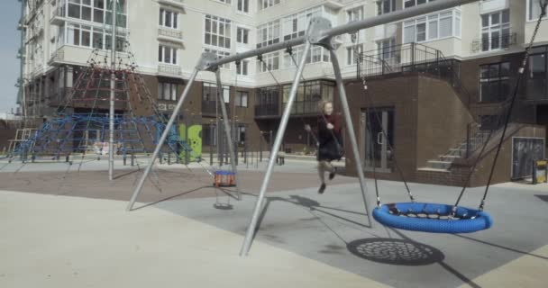 Glimlachende jonge vrouw zwaaien op swing op de speelplaats in de stad. — Stockvideo