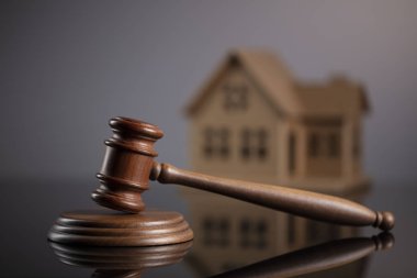 İnşaat Hukuku kavramı. Ev modeli ile gri arka plan üzerinde tahta tokmak.
