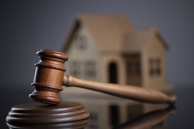 İnşaat Hukuku kavramı. Ev modeli ile gri arka plan üzerinde tahta tokmak.
