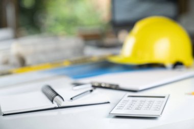 Müteahhit kavramı. Sarı hardhat, libella ve beyaz masa üzerinde planları.