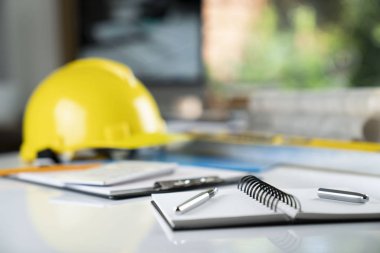 Müteahhit kavramı. Sarı hardhat, libella ve beyaz masa üzerinde planları.