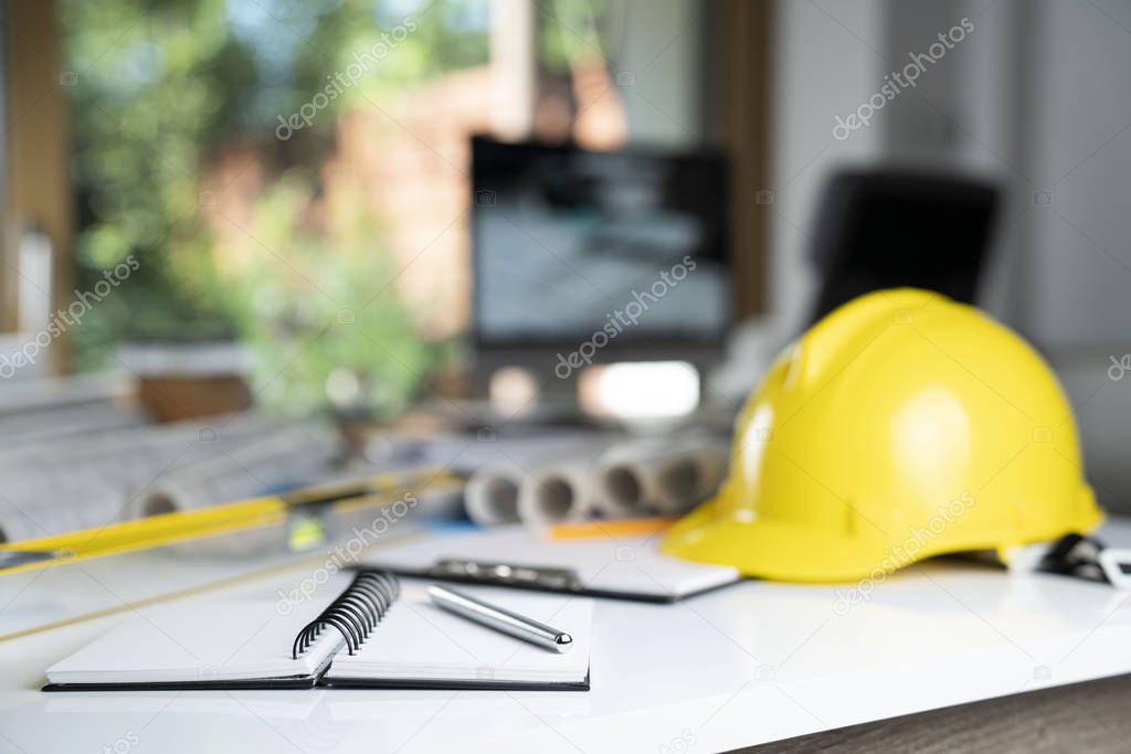 Contractor concept. Yellow hardhat, libella and plans on the white table.