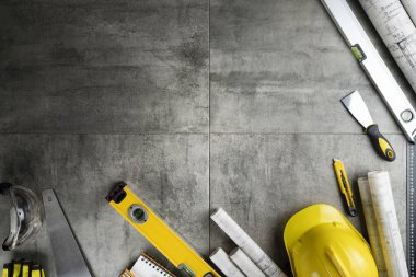 Contractor theme. Rolls with building projects, tools, crash helmet and spirit level on stone background.