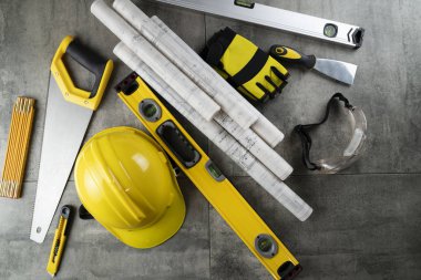 Contractor theme. Rolls with building projects, tools, crash helmet and spirit level on stone background.