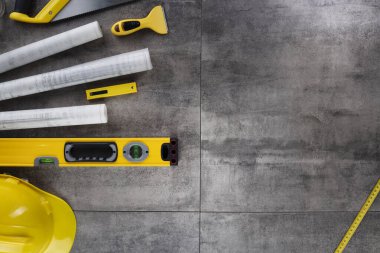 Müteahhit konsepti. Müteahhidin alet çantası, sarı başlık, libella, el testeresi. Gri karoların arka planındaki planlar ve defterler.
