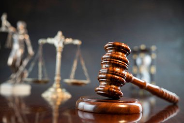 Hukuk sembolleri kompozisyonu. Heykel, hakimler tokmak ve adalet terazisi parlak kahverengi masa ve gri arka plan üzerinde.