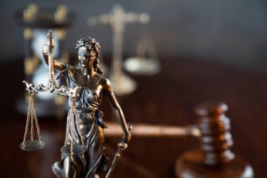 Hukuk sembolleri kompozisyonu. Heykel, hakimler tokmak ve adalet terazisi parlak kahverengi masa ve gri arka plan üzerinde.