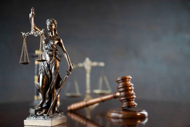 Hukuk sembolleri kompozisyonu. Heykel, hakimler tokmak ve adalet terazisi parlak kahverengi masa ve gri arka plan üzerinde.