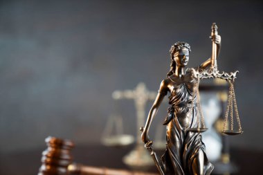 Hukuk sembolleri kompozisyonu. Heykel, hakimler tokmak ve adalet terazisi parlak kahverengi masa ve gri arka plan üzerinde.