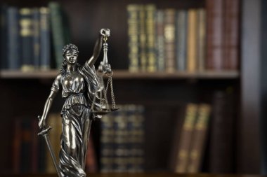 Hukuk teması. Yargıç odası. Kahverengi masadaki heykel. Kitaplıkta yasal kitap koleksiyonu.