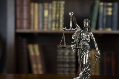 Hukuk teması. Yargıç odası. Kahverengi masadaki heykel. Kitaplıkta yasal kitap koleksiyonu.