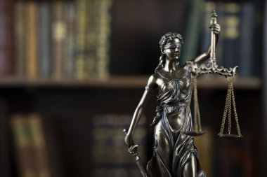 Hukuk teması. Yargıç odası. Kahverengi masadaki heykel. Kitaplıkta yasal kitap koleksiyonu.