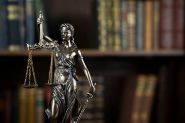 Hukuk teması. Yargıç odası. Kahverengi masadaki heykel. Kitaplıkta yasal kitap koleksiyonu.