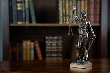 Hukuk teması. Yargıç odası. Kahverengi masadaki heykel. Kitaplıkta yasal kitap koleksiyonu.