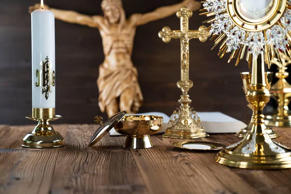 Catholic religion symbols. The Cross, monstrance, Jesus figure, Holy Bible and golden chalice on the rustic wooden altar.