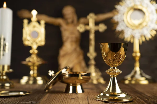 Catholic religion symbols. The Cross, monstrance, Jesus figure, Holy Bible and golden chalice on the rustic wooden altar.