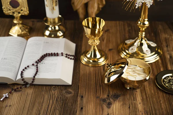 Catholic religion symbols. The Cross, monstrance, Jesus figure, Holy Bible and golden chalice on the rustic wooden altar.