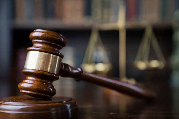 Law theme. Judge chamber. Gavel and scale on brown shining desk. Collection of legal books in the bookshelf.