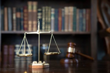 Hukuk teması. Yargıç odası. Gavel ve terazi kahverengi masada. Kitaplıkta yasal kitap koleksiyonu.