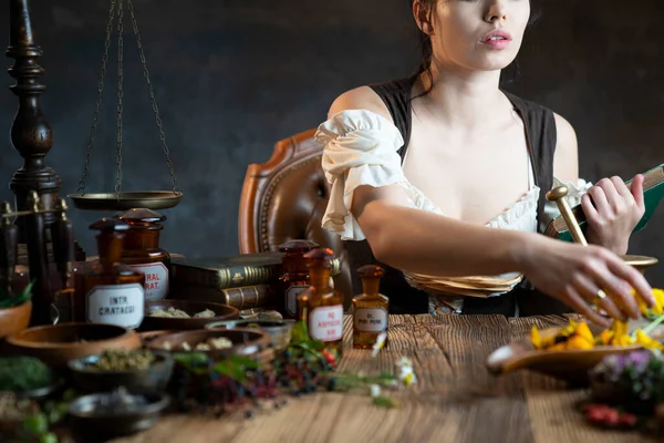 Natural medicine concept. Vintage pharmacist preparing natural medicament. Brass mortar and  bottles. Rustic table. Assorted dry herbs in bowls.