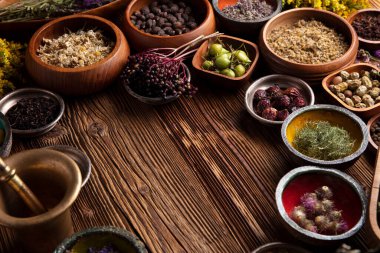 Doğal tıp geçmişi. Kâselerde çeşitli kuru otlar ve rustik ahşap masa üzerinde pirinç havan..