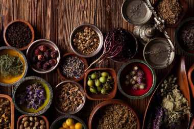 Natural medicine background. Assorted dry herbs in bowls and brass mortar on rustic wooden table.