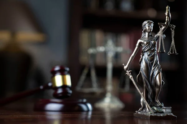 Law theme. Judge chamber. Themis, gavel and scale on brown shining desk. Collection of legal books in the bookshelf.