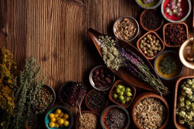 Doğal tıp teması. Kâselerde çeşitli kuru otlar ve rustik ahşap masa üzerinde pirinç havan..