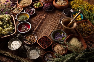 Doğal tıp teması. Kâselerde çeşitli kuru otlar ve rustik ahşap masa üzerinde pirinç havan..