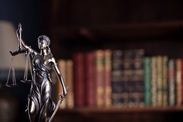 Law and justice concept. Themis sculpture in lawyers office. Bookshelf with legal books in background.