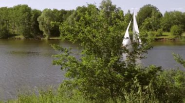 Defne nehir ve yat yavaş geçiş. Kıyıda olan ağaçlar ve çalılar, açık bir gökyüzü.