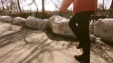 Mutlu kadın şehrin kaldırım boyunca yürüyüş bir kırmızı ceketli. Erken Bahar ve su birikintileri. Kompozisyon bel. Yüzü görünür değil.