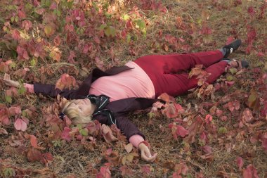 Sonbahar başlarında ormanda mutlu orta yaşlı bir kadın var. Pembe kıyafetler. Çim üzerinde yatıyor. Etrafında büyük pembe yaprakları vardır.