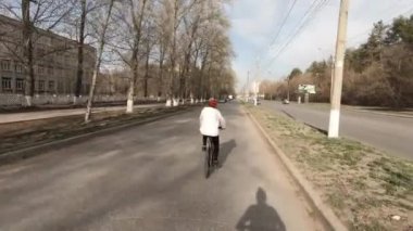 Kırmızı şapkalı orta yaşlı bir kadın. Şehirde bir pistte bisiklete binmek. Arkadan hızla çekim.