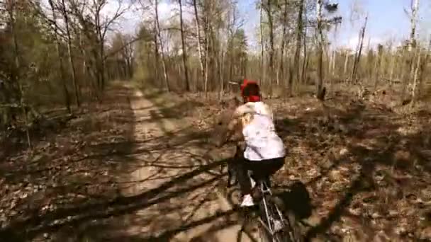 赤い帽子をかぶった中年の女性彼は森の小道に沿って自転車に乗る 晴れの日 速度で後ろから撮影 — ストック動画