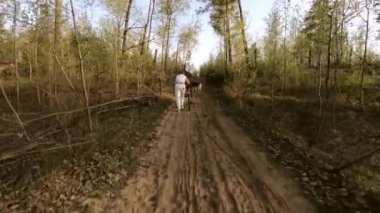 Orta yaşlı bir kadın ıslak kumüzerinde bir bisiklet yokuş yukarı iter. Yakınlarda tasmalı bir köpek var. Yolda ormanda bulunan. Tam büyüme de arkadan çekim.