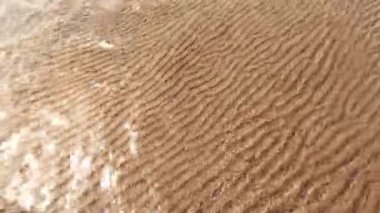 Yaz gününde sahile. Islak, nervürlü kum güneşte parlar. Berrak su ve küçük dalgalar.