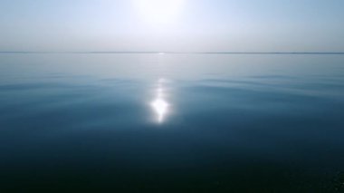 Akşam günbatımı ve parlak bir yansıma, sakin deniz ve pürüzsüz su, pus ufukta, tekne hareketinden sprey. Metin alanı. Atmosferik video.