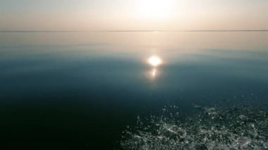 Akşam günbatımı ve parlak bir yansıma, sakin deniz ve pürüzsüz su, pus ufukta, tekne hareketinden sprey. Metin alanı. Atmosferik video.