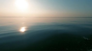 Akşam günbatımı ve parlak bir yansıma, sakin deniz ve pürüzsüz su, pus ufukta, tekne hareketinden sprey. Metin alanı. Atmosferik video.