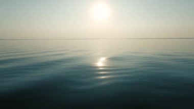 Akşam günbatımı ve parlak bir yansıma, sakin deniz ve pürüzsüz su, pus ufukta, tekne hareketinden sprey. Metin alanı. Atmosferik video.
