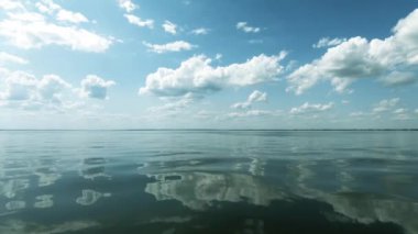 Denizde tekne ile hareket. Bir taraftan çekim. Temiz hava, sakin ve pürüzsüz dalgalar. Suya yansıyan yüksek beyaz bulutlar. Metin alanı. Atmosferik video.