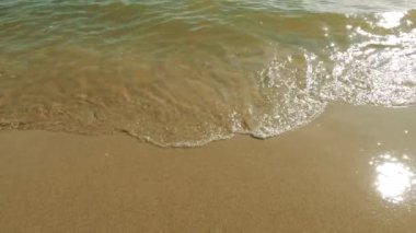 Saf sarı kum ve berrak su küçük dalgalar. Kadın yalınayak gidiyor. Yakın çekim ve sadece bacaklar görünür. Yavaş çekim. Atmosferik video.