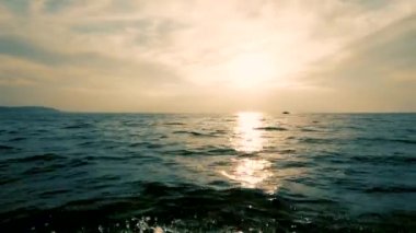 Denizde tekne yle hareket. Bir taraftan ateş etmek. Günbatımı. Kıyının karanlık silueti. Uzak ufku, temiz havayı ve dalgaları, su sıçratan suları görebilirsiniz. Metin için boşluk. Atmosferik video . Uzakta bir tekne yüzüyor..