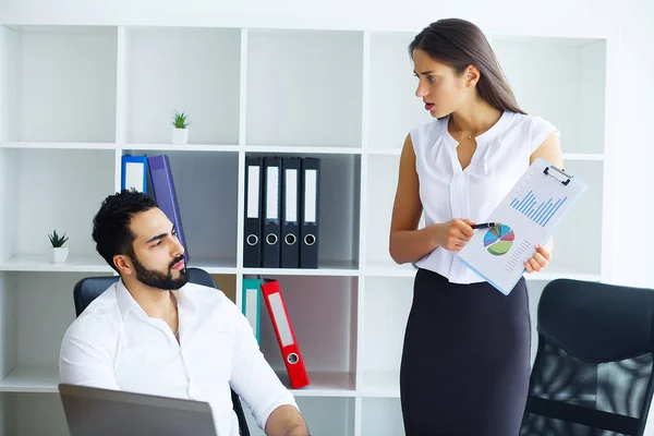 Conflict at work. Nice unhappy scared man sitting on the chair and looking at his colleague while having a conflict with her