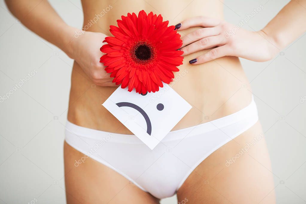 Slim woman dressed in white panties, holding a red flower in her hands, close-up. Gynecology, menstruation, the concept of genital health