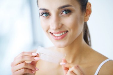 Diş beyazlatma. Şerit beyazlatma tutan güzel gülümseyen kadın. Yüksek çözünürlüklü görüntü